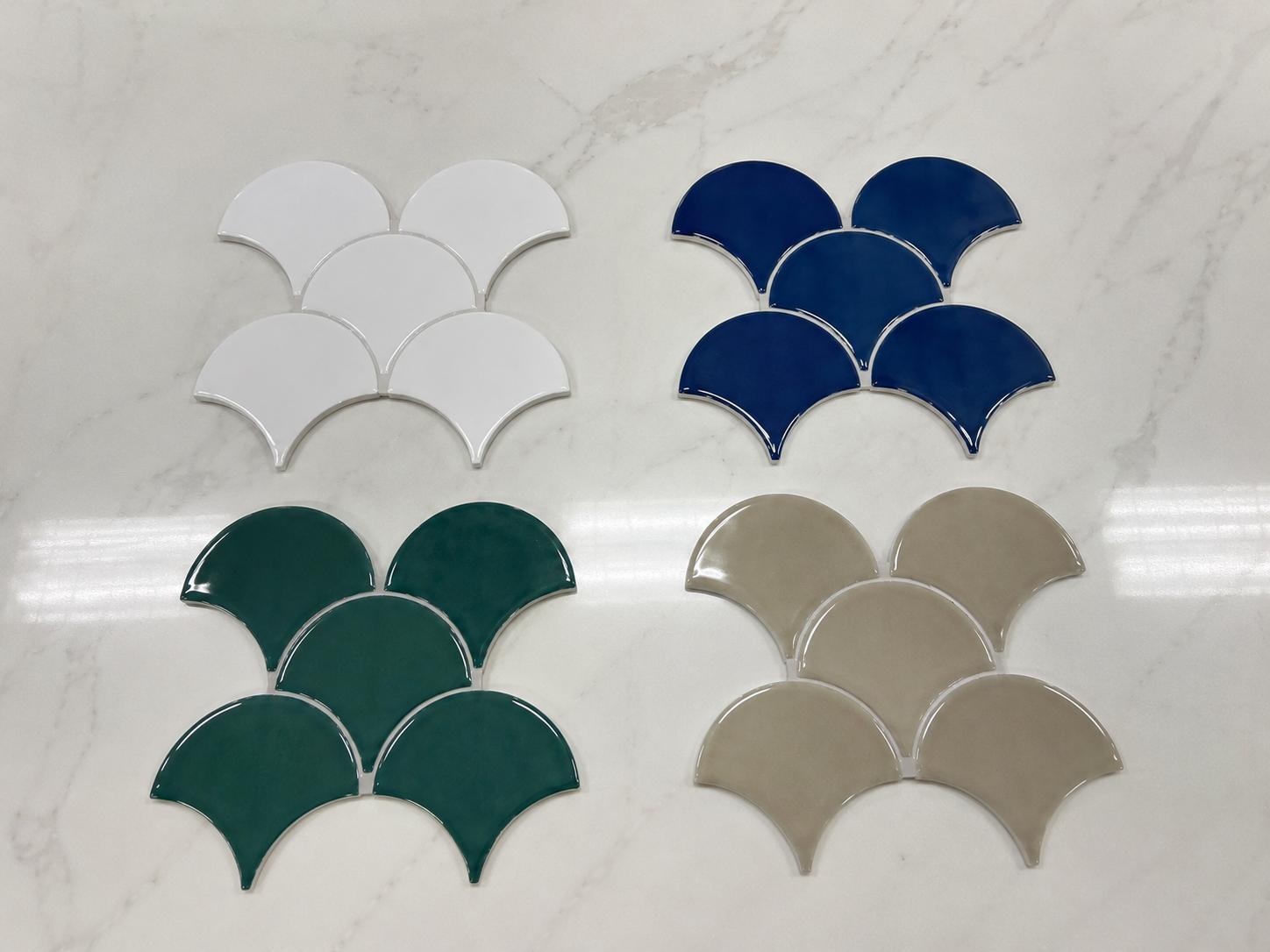 Scalloped tile samples in white, blue, green, and beige displayed on a marble surface